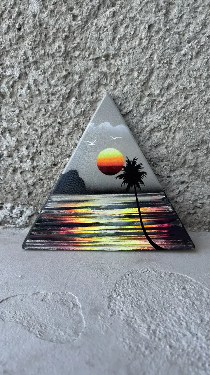 Triangle painting of a grey sky and a colourful sunset reflected on the water with a palm tree