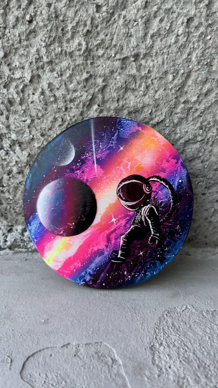 Circle painting of an astronaut floating near a planet in a pink and purple nebula