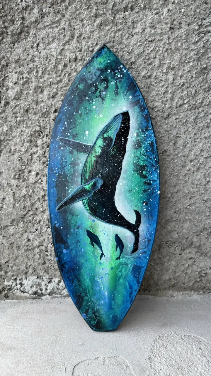 Surfboard-shaped painting of a whale and two calves in glowing green and blue water